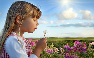 girl holding white Dandelion while blowing during daytime HD wallpaper
