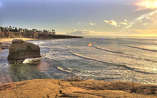 rocky cliff on shore rippling body of water during golden hour HD wallpaper