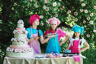 three woman wearing aprons standing in front 3-tier floral cake HD wallpaper
