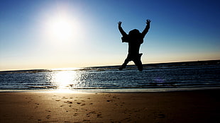 silhouette of man hopping on seashore HD wallpaper
