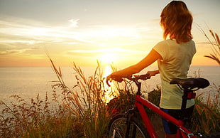 woman in white cap-sleeved shirt holding red mountain bike under golden hour HD wallpaper