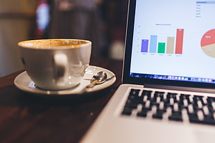 white ceramic coffee cup beside laptop