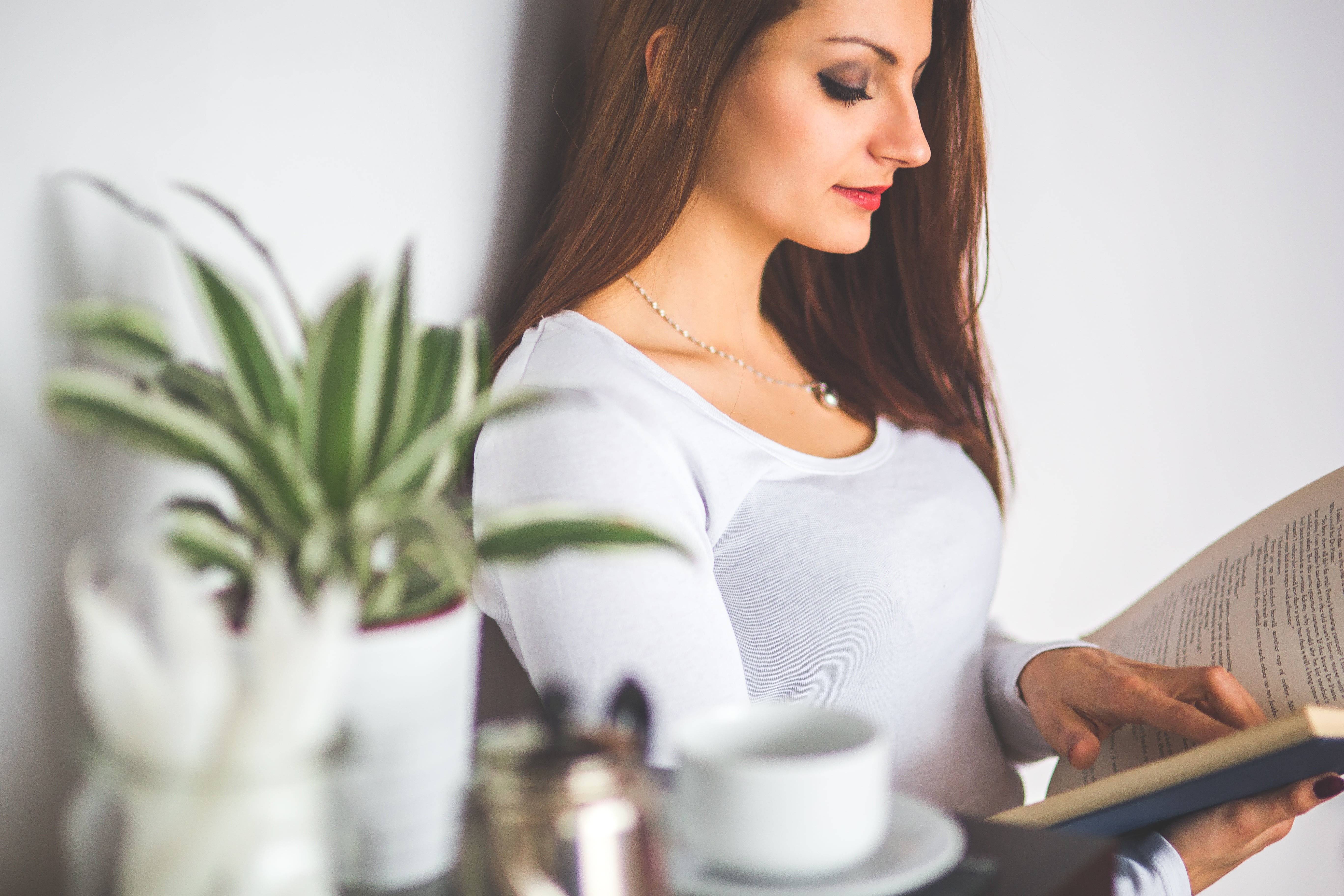 woman reading book sitting on chair beside green potted plant