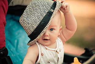 baby in white tank top holding fedora hat