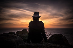 silhouette of person wearing bucket hat near body of water during sunset HD wallpaper