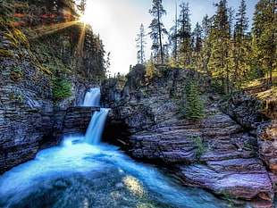 waterfalls in between of rock formation surrounded by trees