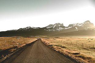 empty road beside open field near mountain covered with snow during daytime HD wallpaper