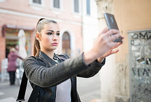 woman wearing black jacket taking selfie during daytime HD wallpaper