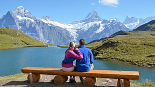 couple sitting in front of body of water and snow mountain during daytime HD wallpaper