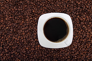 coffee in white cup on ceramic saucer with full of coffee beans