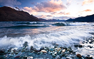 high-saturated photography of sea waves and stones under cumulus clouds