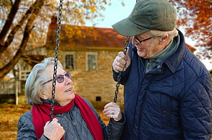 man wearing cap and black jacket in front of woman sitting on swing during daytime