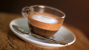 clear glass teacup filled with coffee on white ceramic saucer