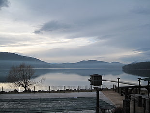 photo of shed on lake near mountains with cloudy skies