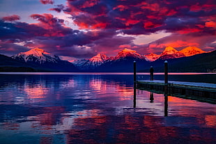 people standing on brown dock surrounded of body of water under orange sunset