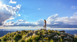 woman wearing white dress standing on cliff with rocks and grasses during daytime with cloudy sky