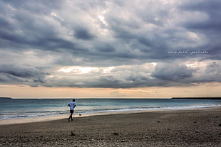 man walking on seashore under blue cloudy skies HD wallpaper