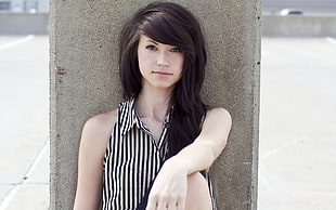 women's black and white pinstriped sleeveless top leaning on gray concrete wall