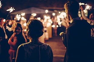 man wearing black suit holding backpack beside woman in sleeveless dress in event during nighttime