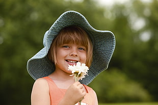girl in gray bucket hat holding white cluster flower during daytime HD wallpaper