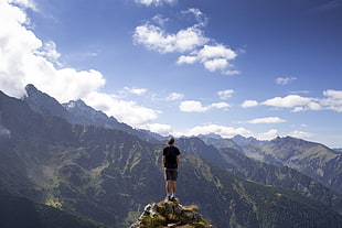 man in black t-shirt standing on mountain cliff under blue sky HD wallpaper