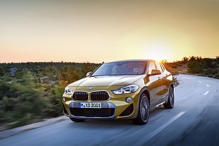 gold BMW 5-door hatchback on grey concrete road during daytime HD wallpaper