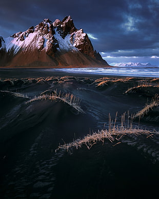 brown and white mountain covered by snow near ocean under grey skies