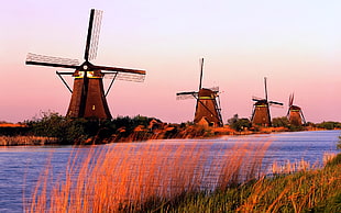 wooden windmills near body of water during sunset HD wallpaper