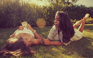 woman wearing white strapless shirt laying on ground near woman wearing white dress shirt planking on ground