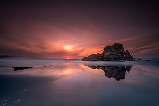 silhouette photography of rocky mountain between body of water during sunset