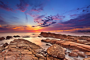 rock formation near body of water during sunset