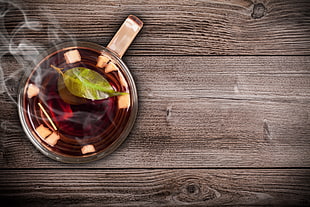 clear glass tea cup with steaming tea on top of brown wooden top