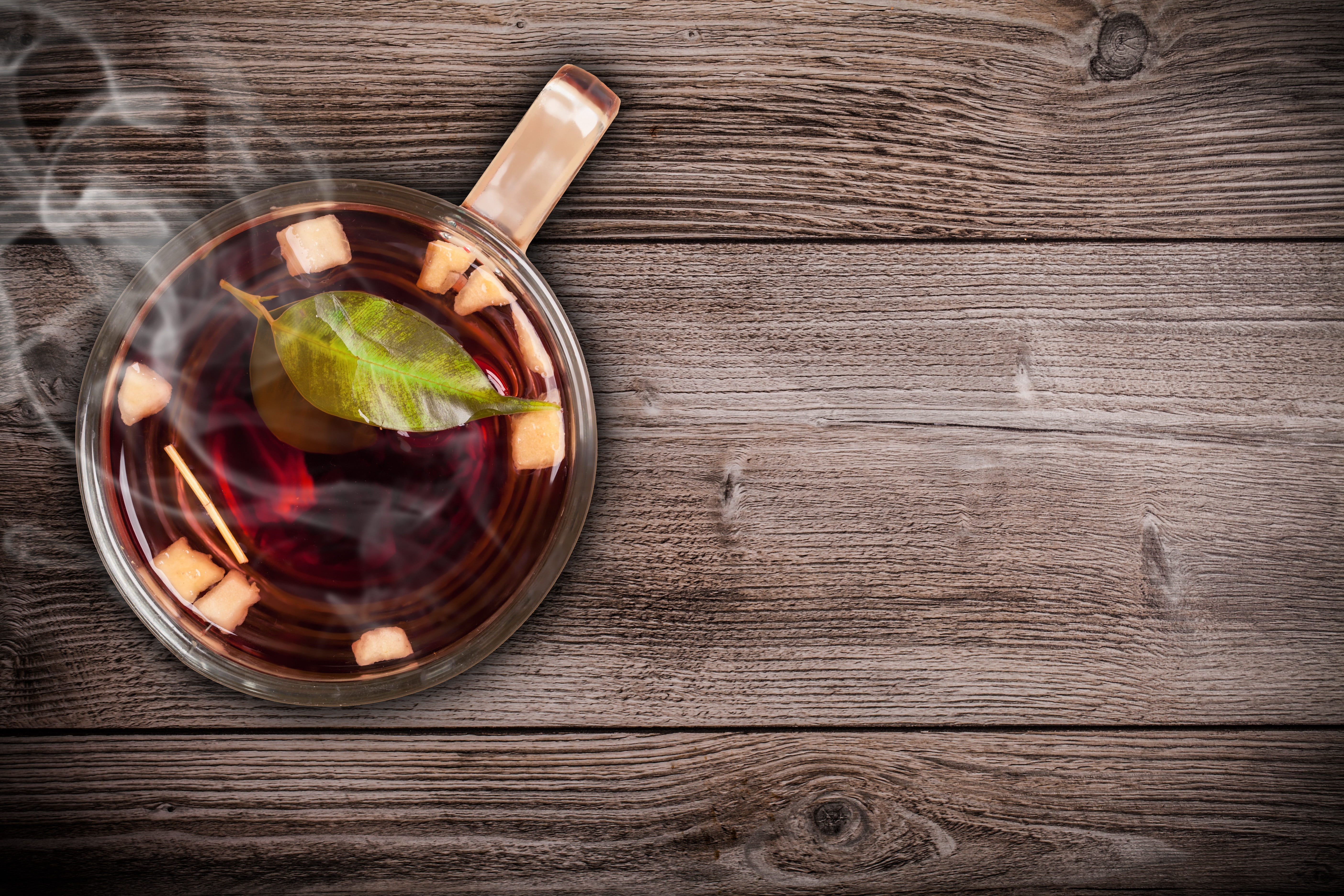 clear glass tea cup with steaming tea on top of brown wooden top