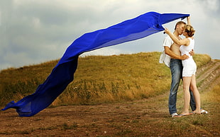 couple kissing on field while holding blue textile HD wallpaper