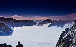 snow coated land between mountains under blue sky