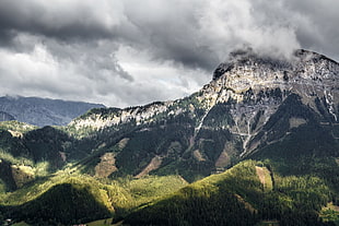 greenfield near rock mountain hills under cloudy sky during daytime