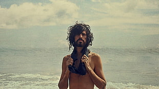 topless man holding textile near beach at daytime