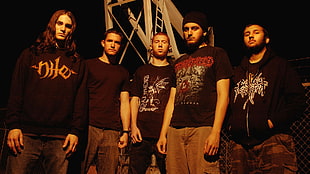 group of men wearing black shirts and brown pants standing near the metal structure