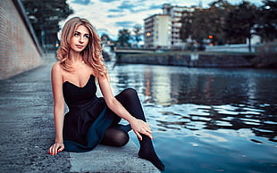 woman wearing black strapless dress sitting beside body of water at daytime HD wallpaper