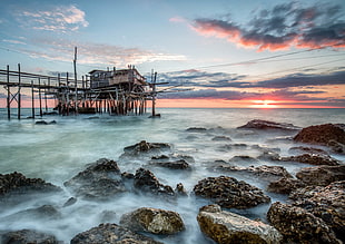 wooden house on body of water with rocks on shore