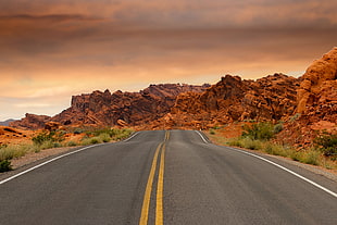 asphalt road with double yellow line near mountains under grey cloudy sky