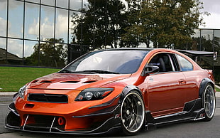 orange and black Scion tC on grey concrete road near green leaf tree and building