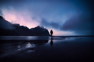 silhouette of man standing on sea during night time HD wallpaper