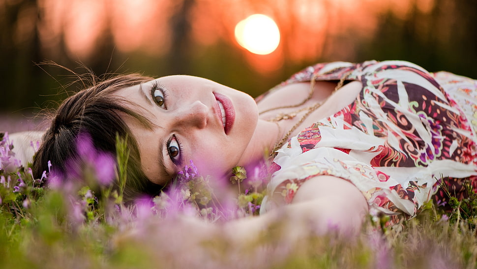 woman wearing white and brown floral scoop-neck top lying on green grass during daytime HD wallpaper