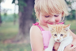 girl in pink sleeveless dress holding brown and white kitten