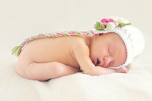 naked baby in white,green and pink knitted  cap lying on white textile HD wallpaper