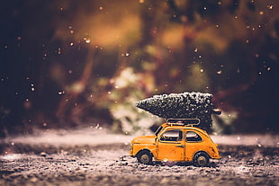 orange die-cast beetle car with pre-lit christmas tree on roof in tilt shift lens photo HD wallpaper