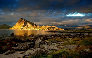 brown mountain near body of water under blue sky HD wallpaper