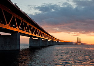 shallow focus photography of bridge surrounded of body of water under orange sunset