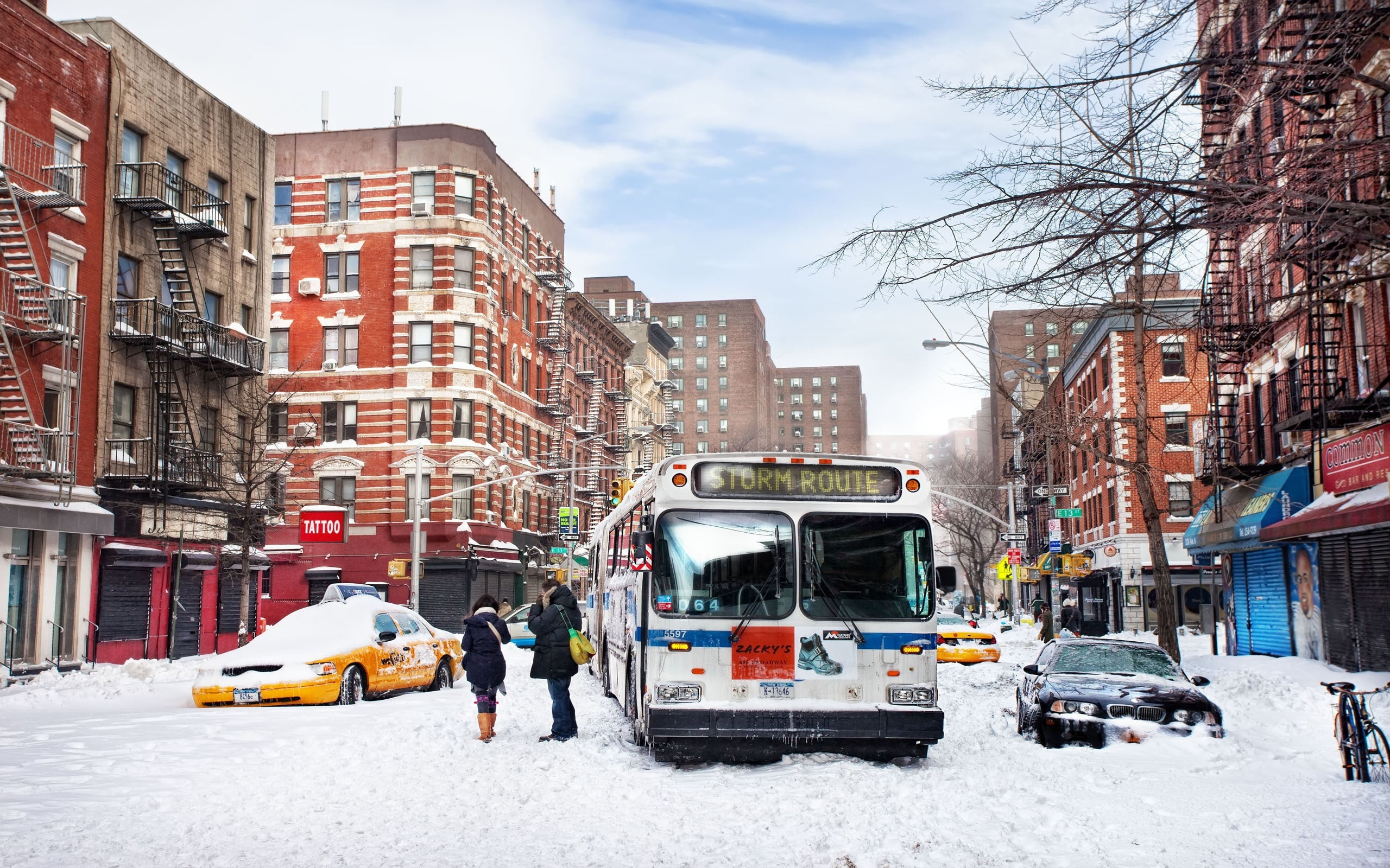 man and woman standing beside bus and taxi during winter season in between high rise buildings